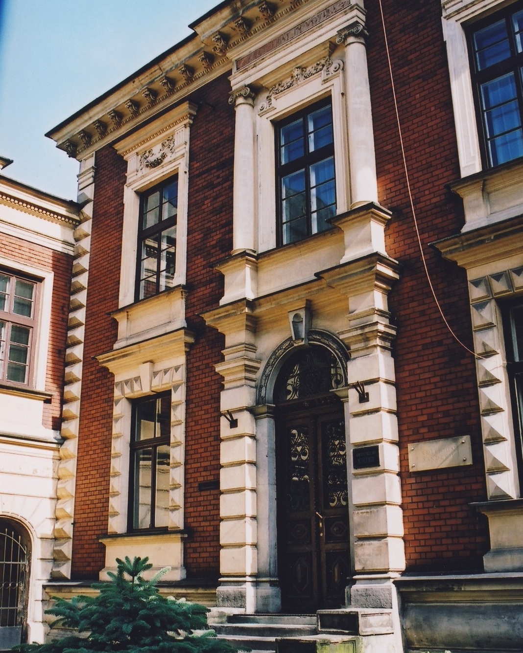 Budynek Instytutu Pedagogiki UJ od strony frontowej. Ozdobny gzyms, wejście główne i okna. Budynek z czerwonej cegły.